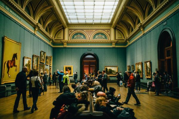 A bustling art gallery with people admiring paintings and architectural details.