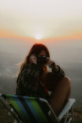 A woman with long hair captures the serene sunset in Mogi das Cruzes, Brazil, embodying tranquility and beauty.