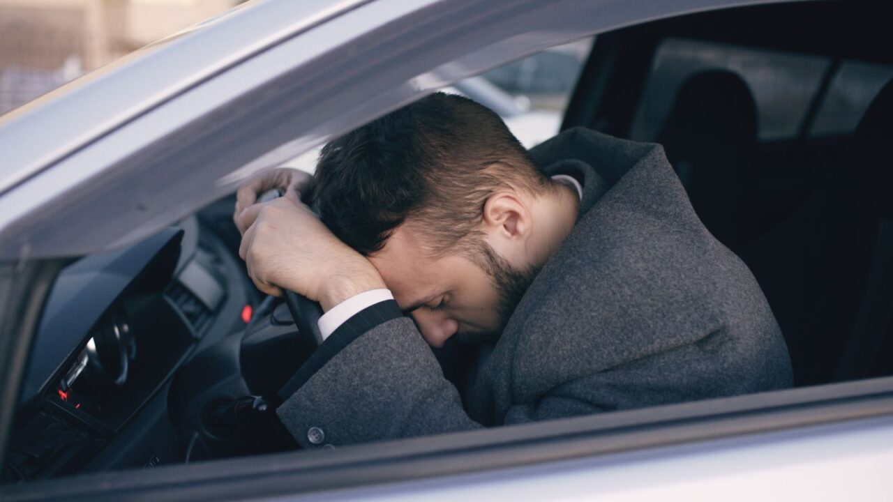 Man in car showing stress with head on steering wheel, highlighting emotional fatigue.
