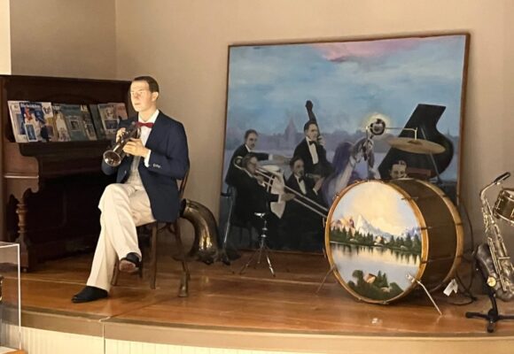 A scene in the new home of the Bix Beiderbecke Museum in downtown Davenport recreates the stage Bix played in 1926, in Hudson Lake, Indiana, with a painting by Bruce Walters of Davenport in the background. Walters painted the mural for a similar scene at the old museum in the lower level of the Redstone Building. (photo by Jonathan Turner)