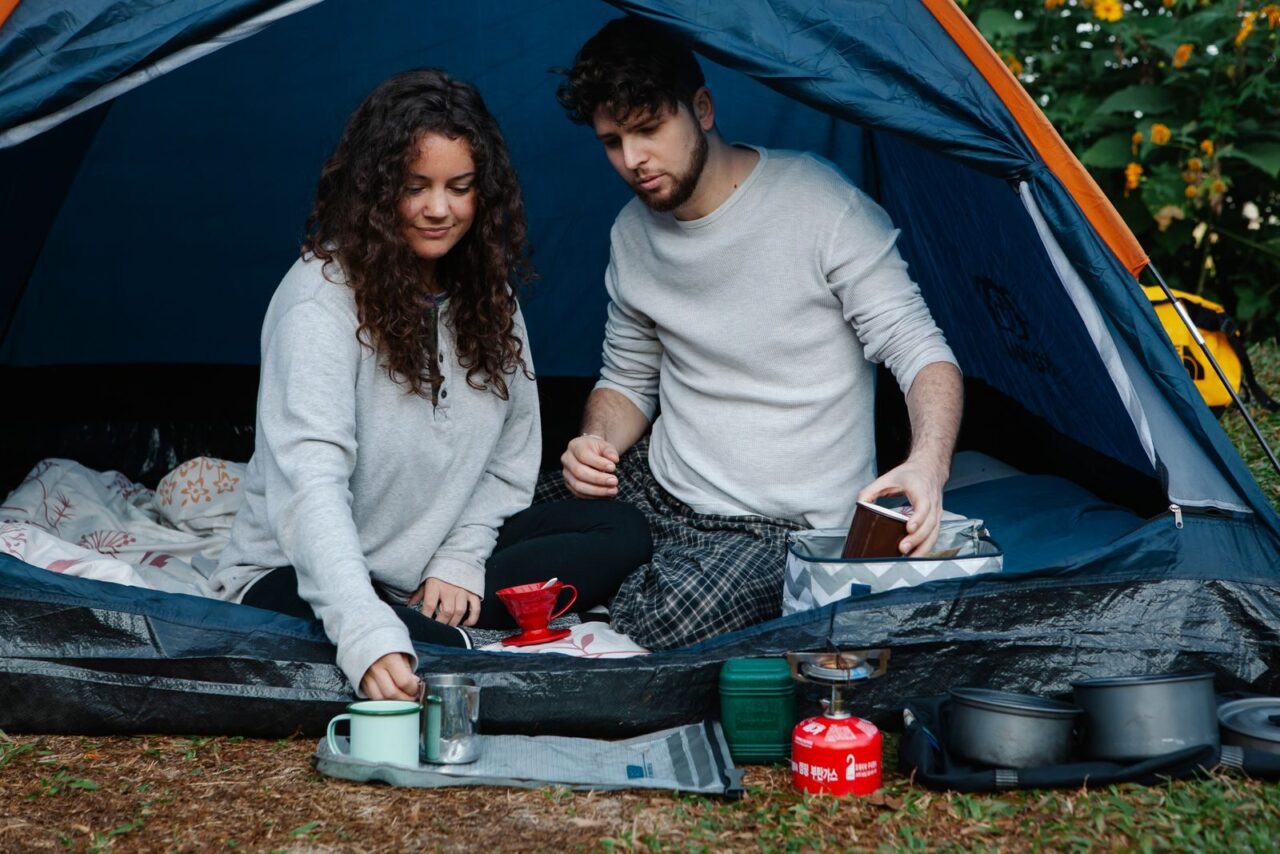 Young smiling couple in pyjamas making breakfast sitting in tent while spending holidays together in countryside