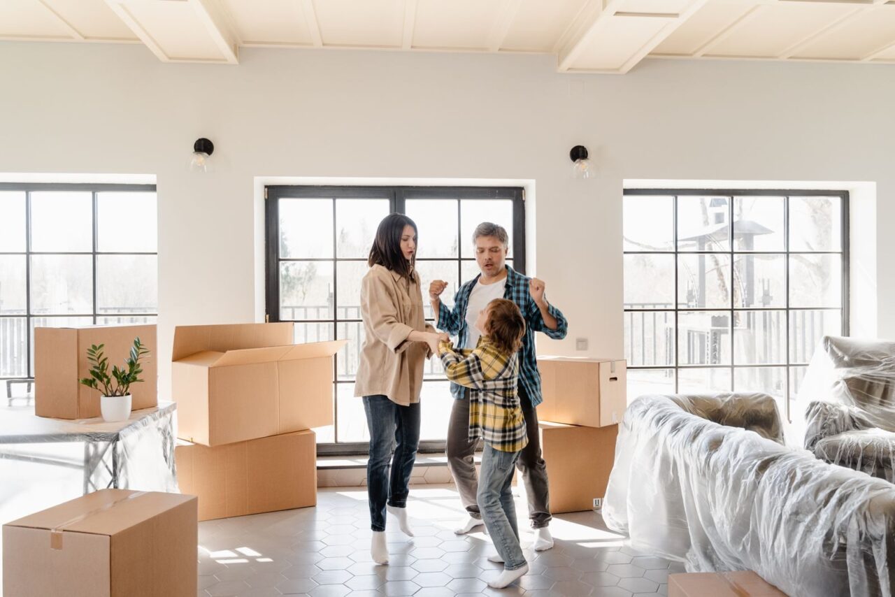 Family joyfully celebrating their new home among moving boxes and furniture.